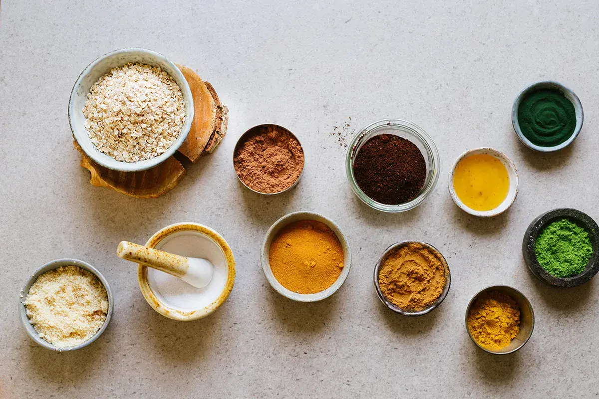 Ingredienser för hemmagjord ansiktsskrubb: havregryn, kakaopulver, kaffesump, gurkmeja, matcha och olja.