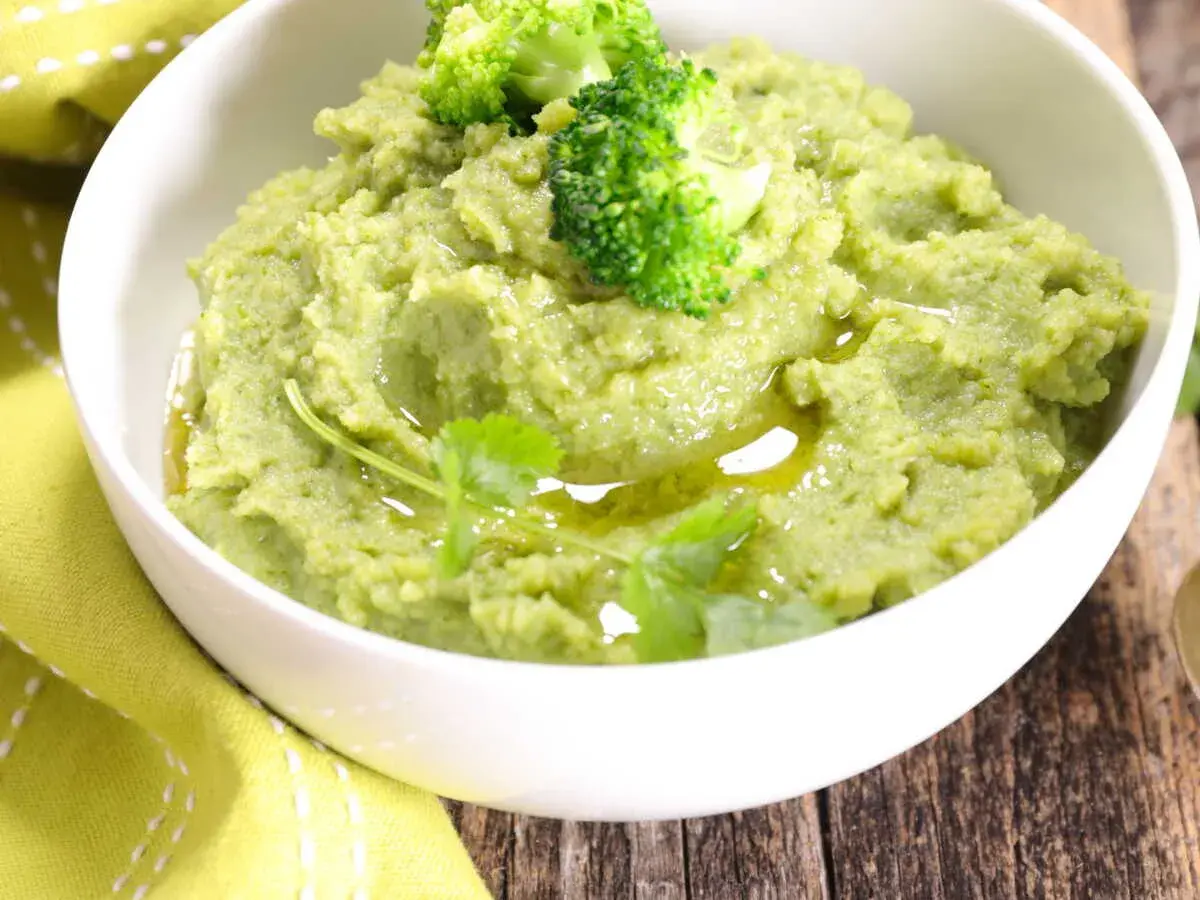 Un bol de purée de brocolis onctueuse, garnie de fleurettes de brocolis et d'un filet d'huile d'olive.