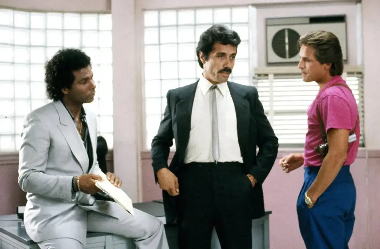 Trzech mężczyzn, w tym policjanci z Miami obsada, w tym Sonny Crockett i Ricardo Tubbs, rozmawiają w biurze.