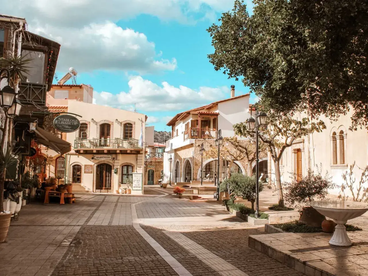 Malia, Kreta: malerische Gasse mit Cafés und traditionellen Gebäuden unter blauem Himmel.