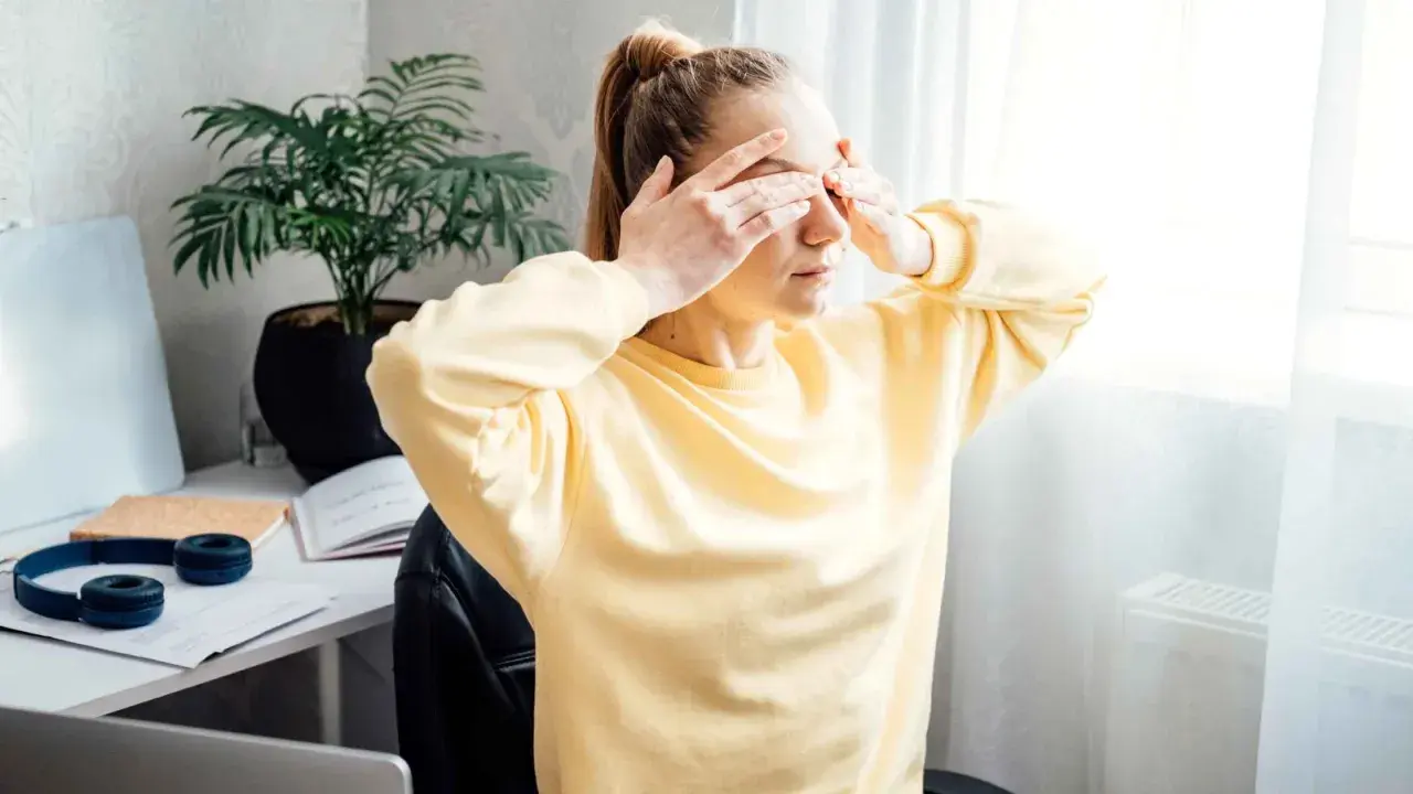 Une jeune femme, le visage marqué par la tension oculaire et le stress, se couvre les yeux.