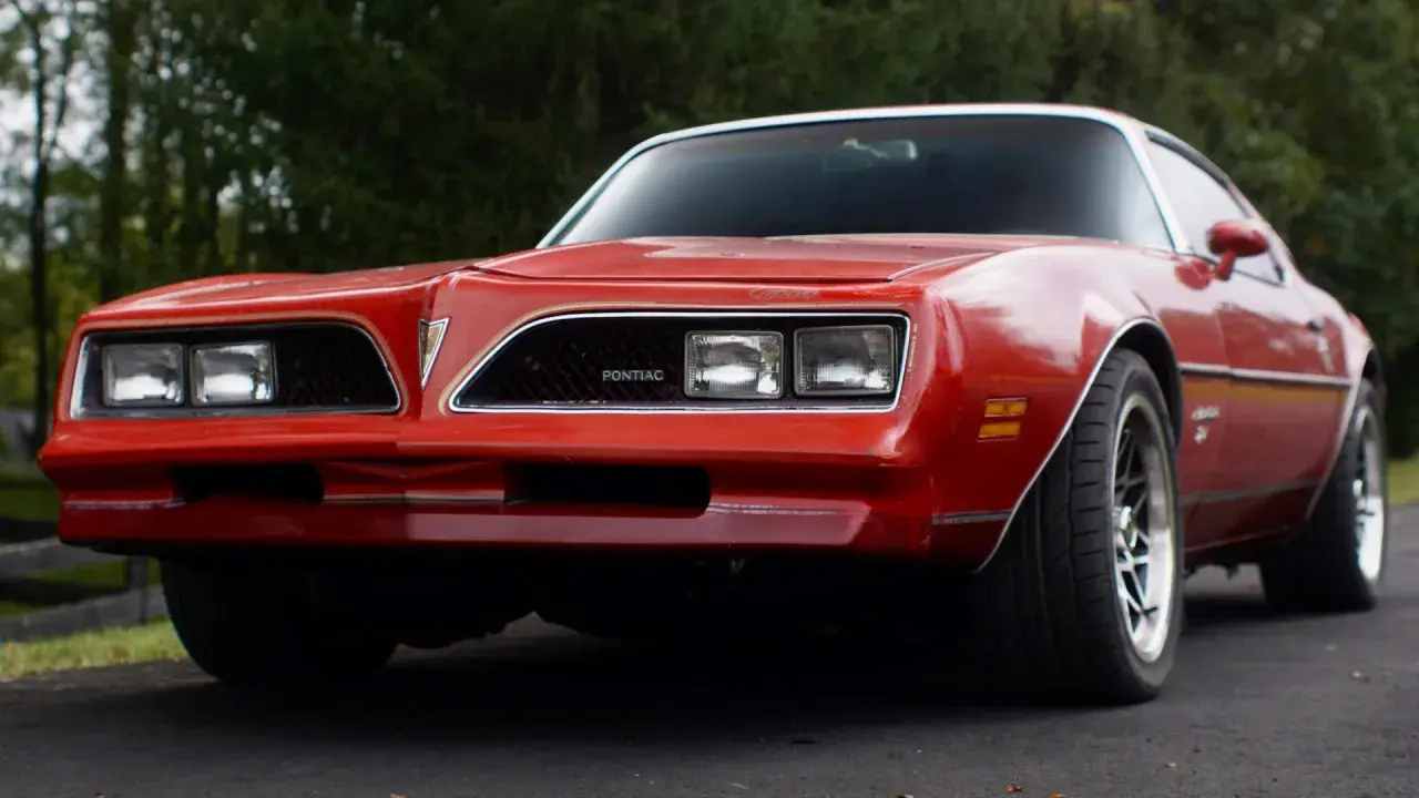 Röd Pontiac Trans Am från 70-talet, med sina karaktäristiska dubbla strålkastare och en ikonisk grill.
