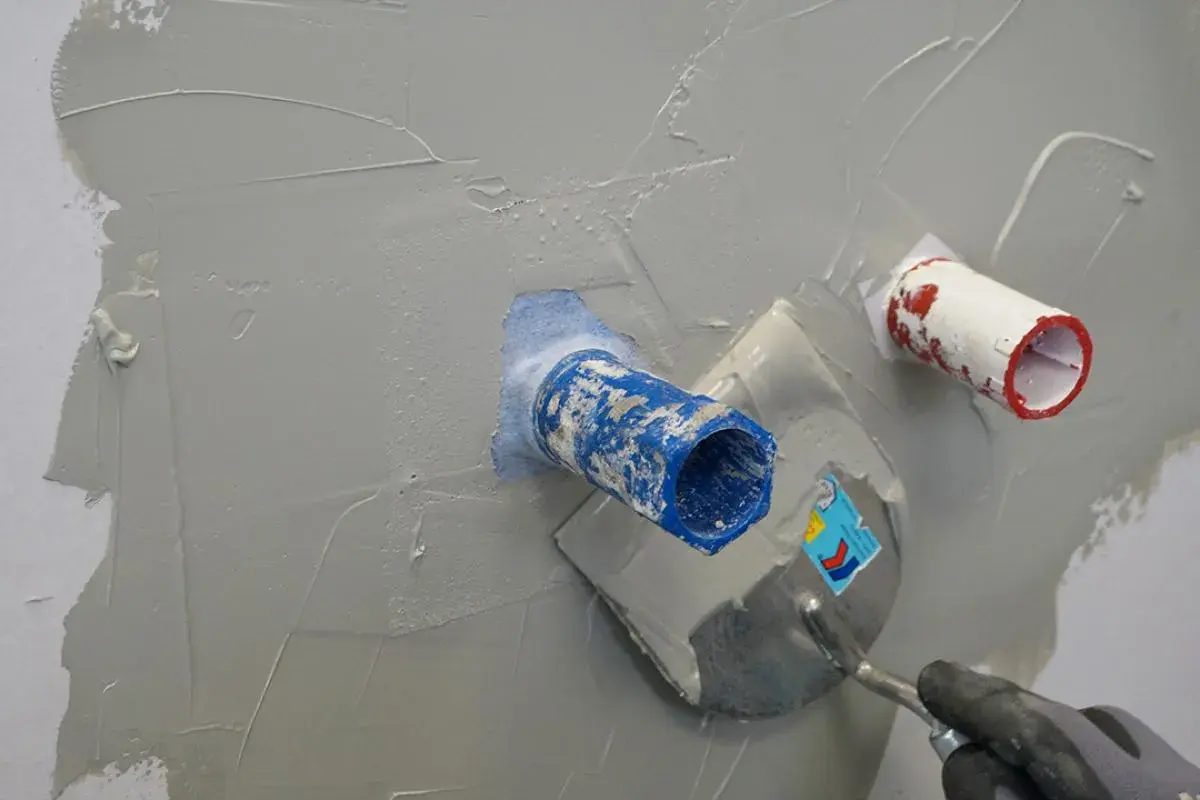 Mit einer Kelle wird graue Masse aufgetragen, um die Rohre in der Wand zu dusche abdichten.