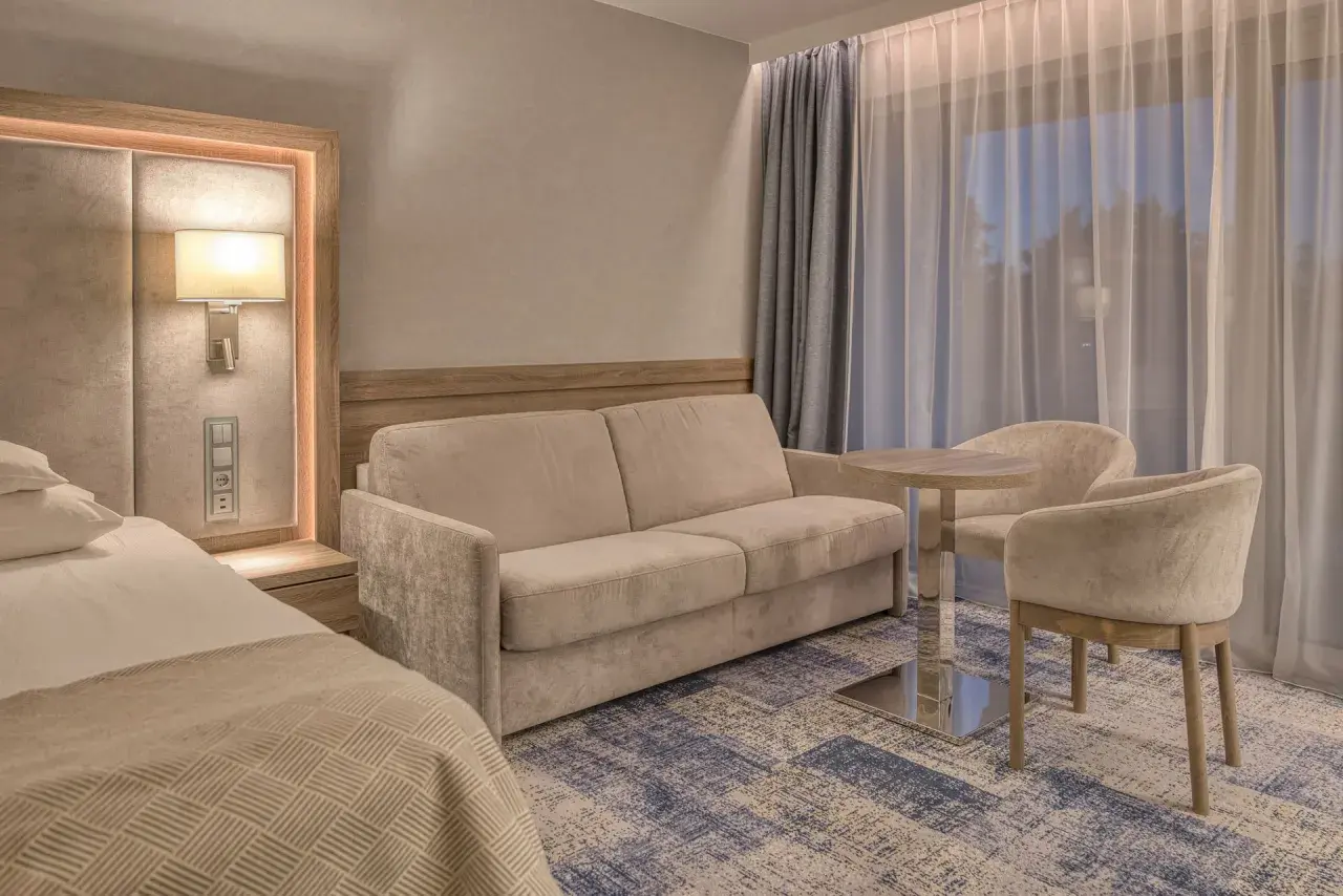 Przytulny pokój w hotelu 5 gwiazdkowym nad morzem: wygodna sofa, stolik z krzesłami i łóżko.