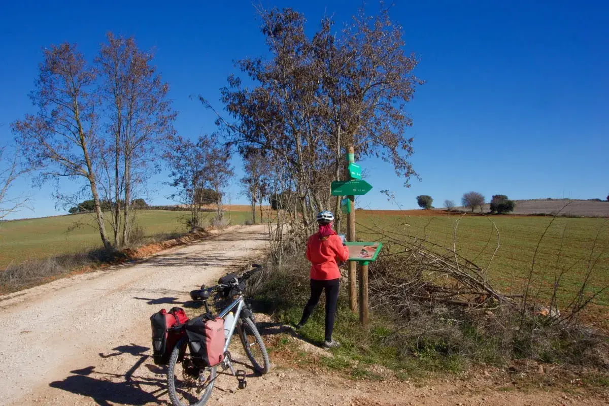 Ciclista consulta señalización en la **vía verde del Tajuña**. Bicicleta con alforjas lista para la aventura.