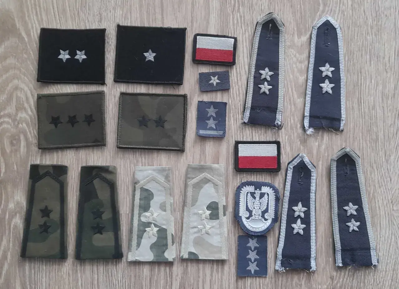 Różne stopnie wojskowe na pagonach i naszywkach, w tym polska flaga.