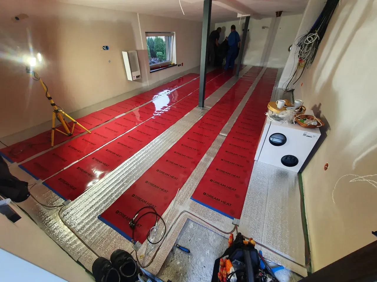 Instalacja folii grzewczej "Dream Heat" na podłodze. Czy folia grzewcza jest oszczędna? Montażyści pracują, przygotowując pomieszczenie do ogrzewania.