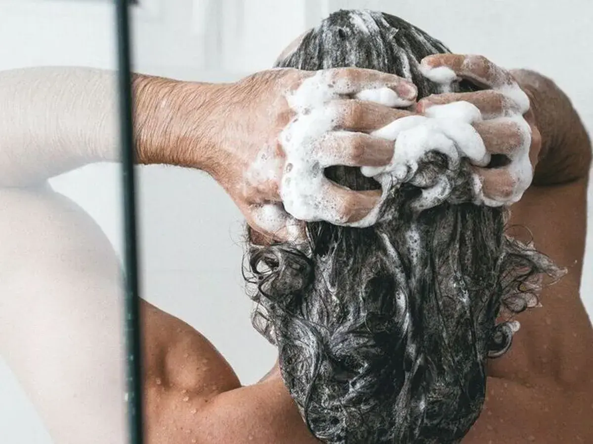 Persona disfrutando de un relajante lavado de cabeza con abundante espuma de champú.