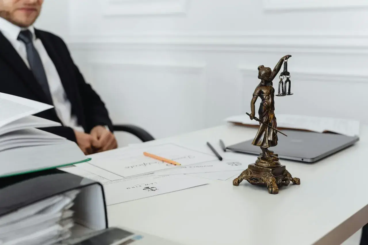 Une statue de la justice, symbole du juge de l'exécution, trône sur un bureau avec des documents et un homme en costume.