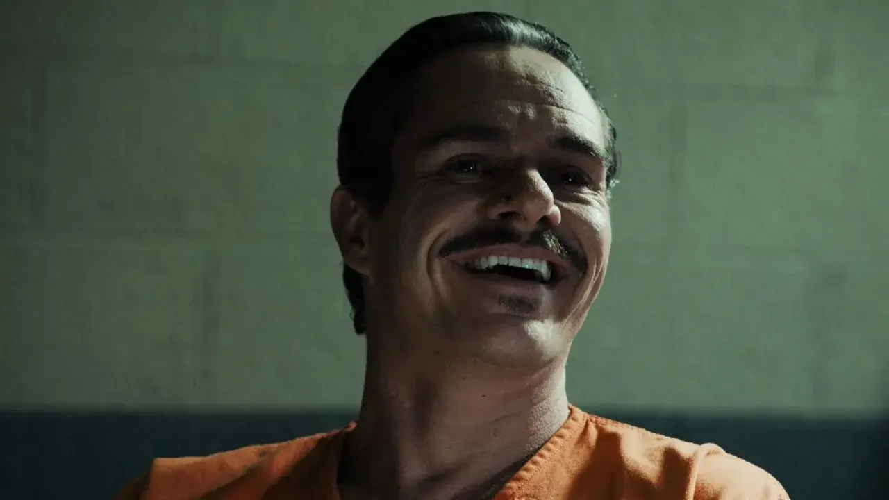Lalo Salamanca ler skrattande i en orange fängelsedräkt, hans mustasch framträder tydligt.