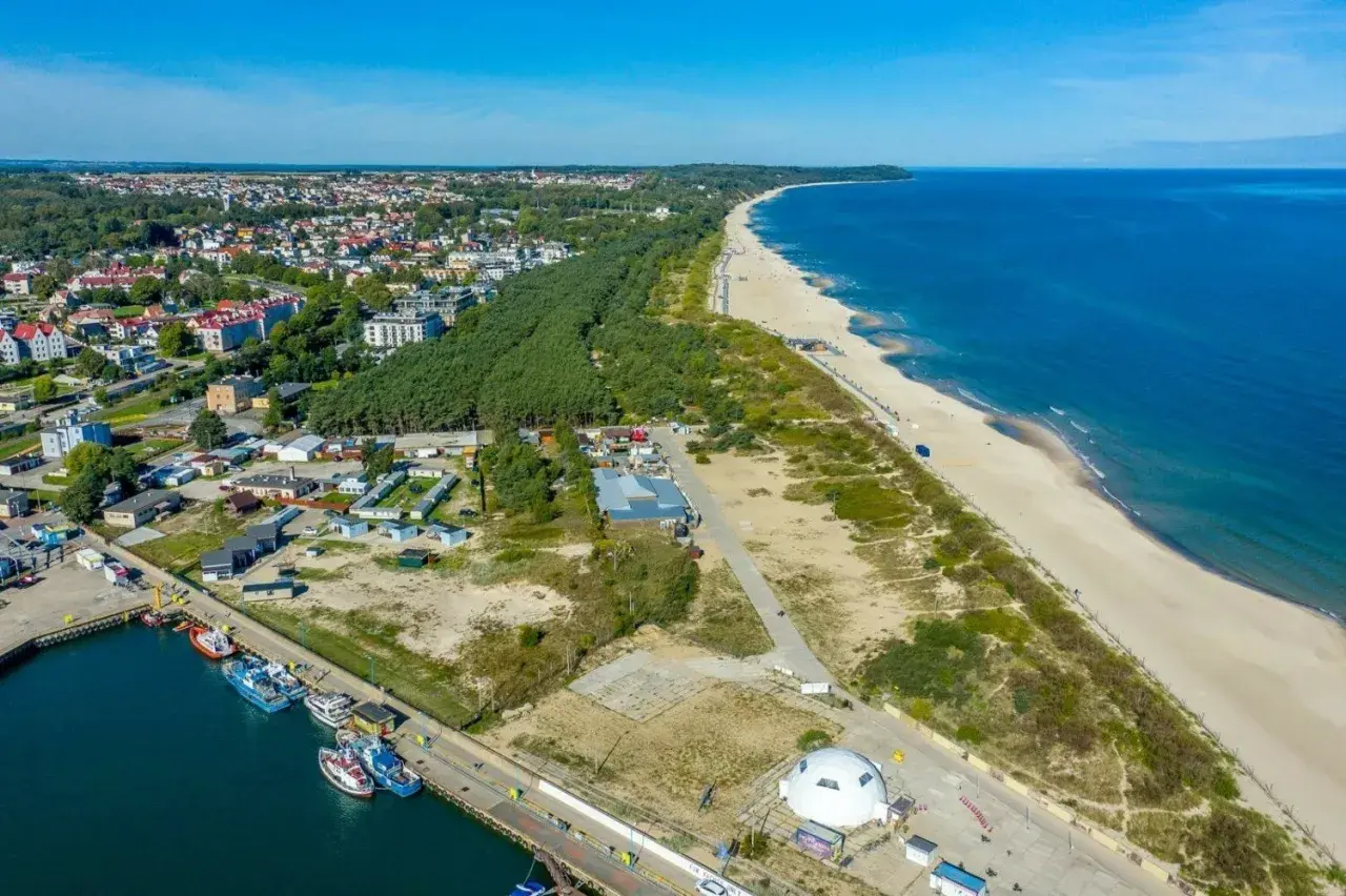 Widok na port i plażę w Władysławowie, z widoczną linią brzegową Jastrzębiej Góry w oddali.