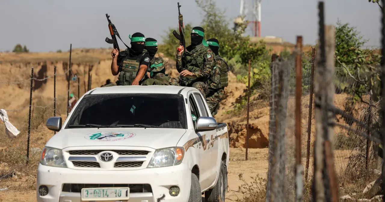 Uzbrojeni bojownicy Hamas w zielonych opaskach na głowach siedzą na białej toyocie, gotowi do akcji.