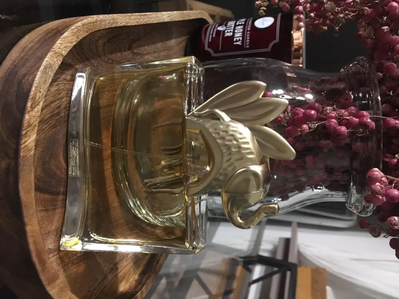 Złoty Kenzo Elephant zdobi flakon perfum, otoczony drewnianą misą i ozdobnymi gałązkami z różowymi owocami.