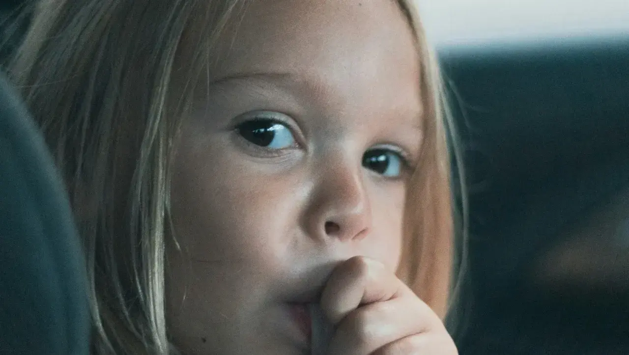 Zamyślona dziewczynka z blond włosami wkłada palec do ust. Może to być oznaka stresu lub nawyku, co na obgryzanie paznokci u dzieci warto sprawdzić.