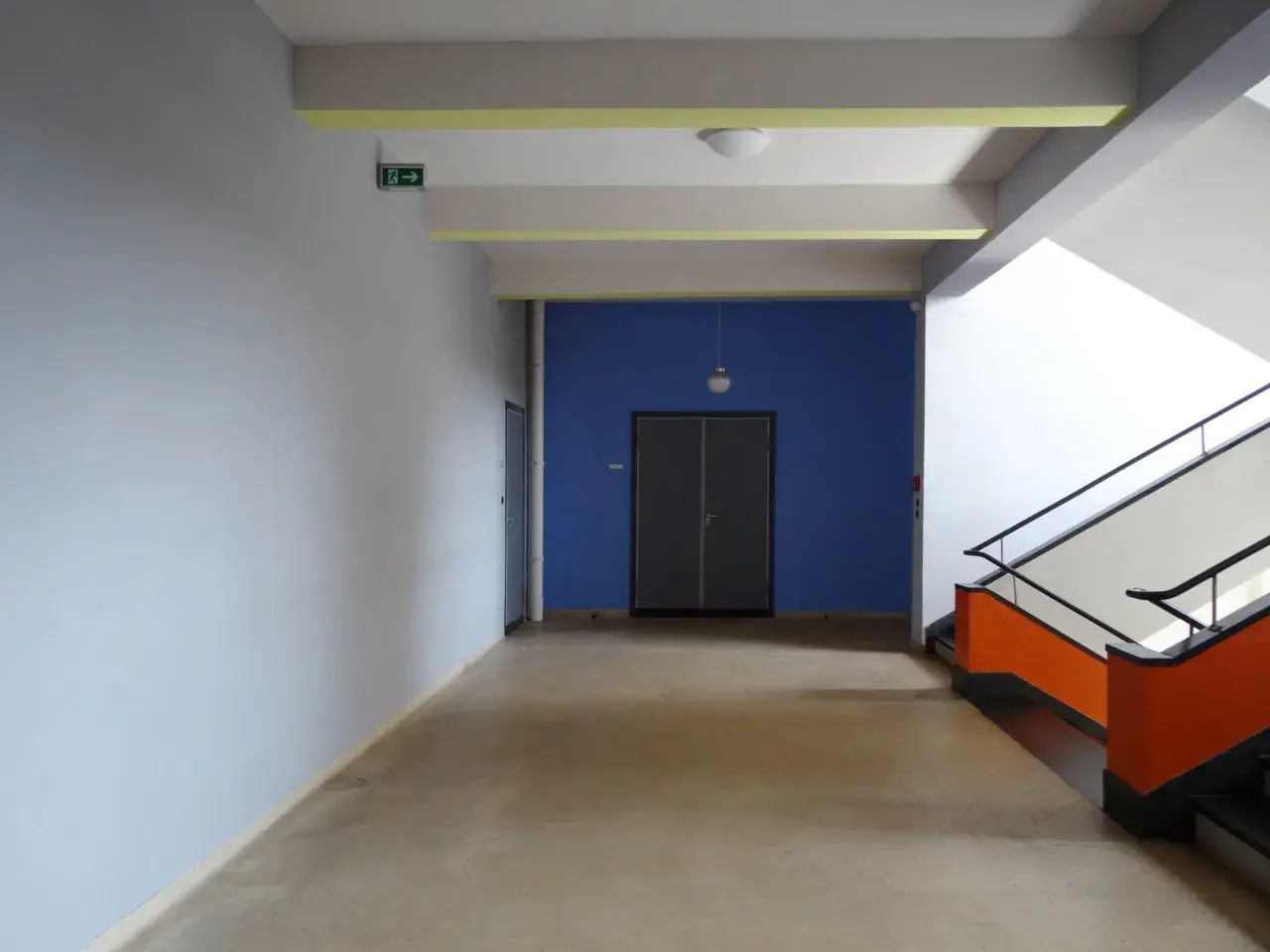Ein Flur mit hellem Estrich, blauer Wand und auffälliger Treppe. Der Boden ist nach DIN-Norm verlegt.