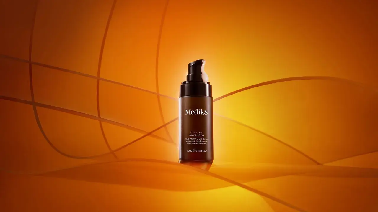 En flaska Medik8 C-Tetra Advanced serum med 20% C-vitamin, en kraftfull antioxidant för din hudvård, står på en orange bakgrund.