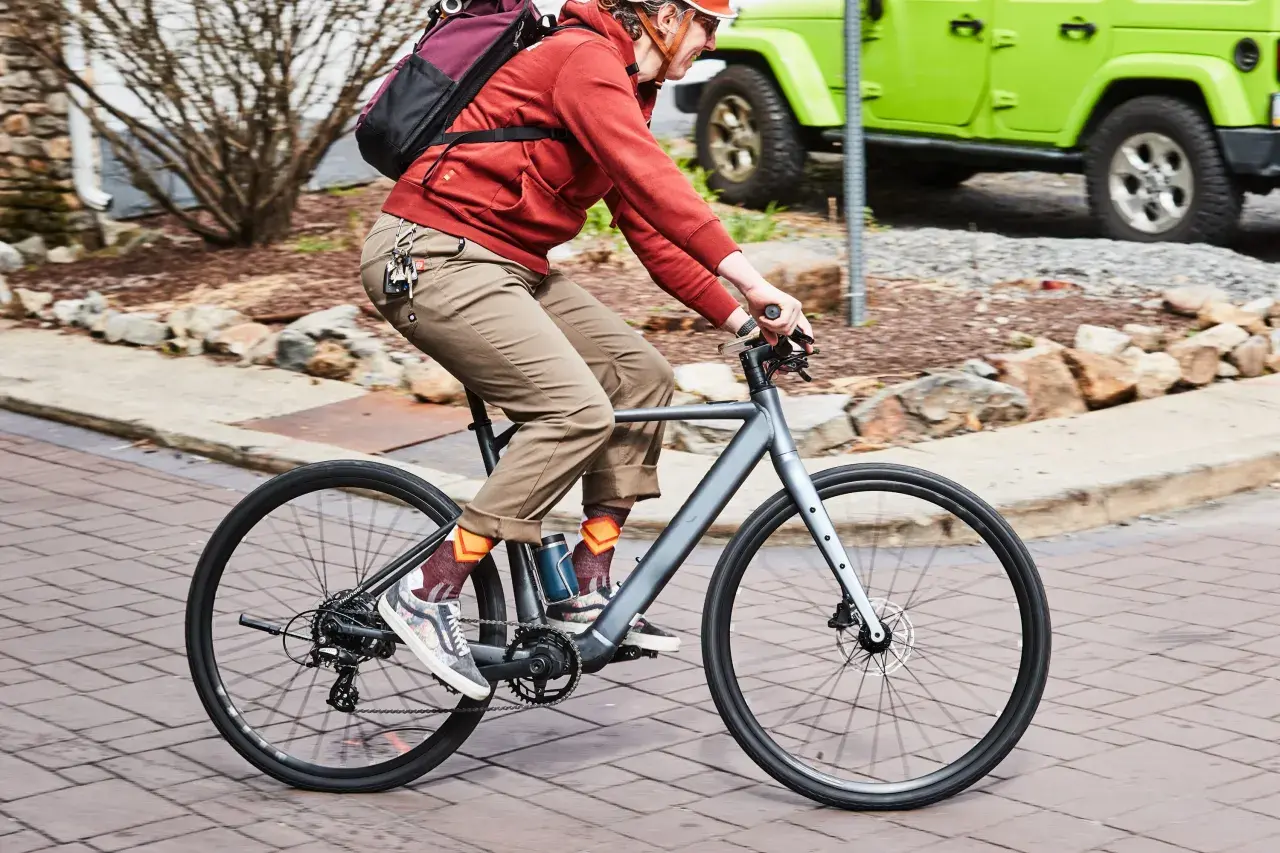 Enjoying the benefits of electric bikes: a person rides a sleek e-bike past a green Jeep, showcasing an eco-friendly commute.
