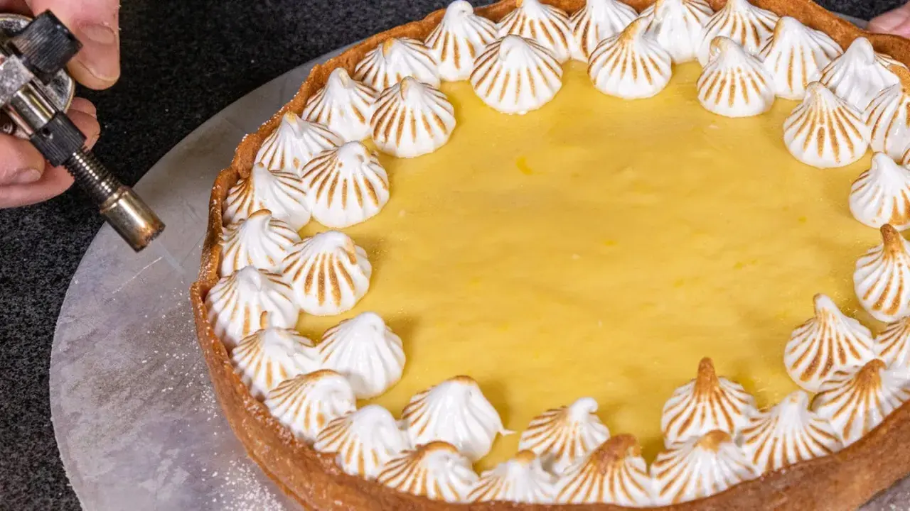 Ein köstlicher Lemon Curd Kuchen mit Baiserhauben wird mit einem Brenner karamellisiert.