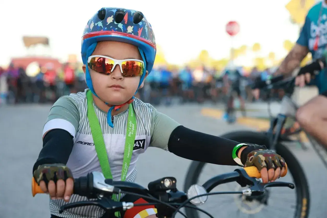Chłopiec w kasku rowerowym i okularach przeciwsłonecznych, gotowy do jazdy. Czy kask na rower jest obowiązkowy? Ten młody cyklista pokazuje, że bezpieczeństwo jest ważne.
