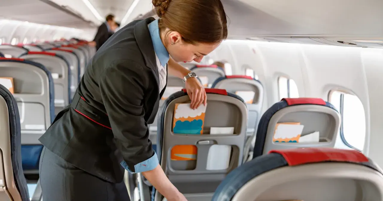 Uśmiechnięta stewardessa przygotowuje kabinę samolotu, układając materiały w kieszeniach foteli.