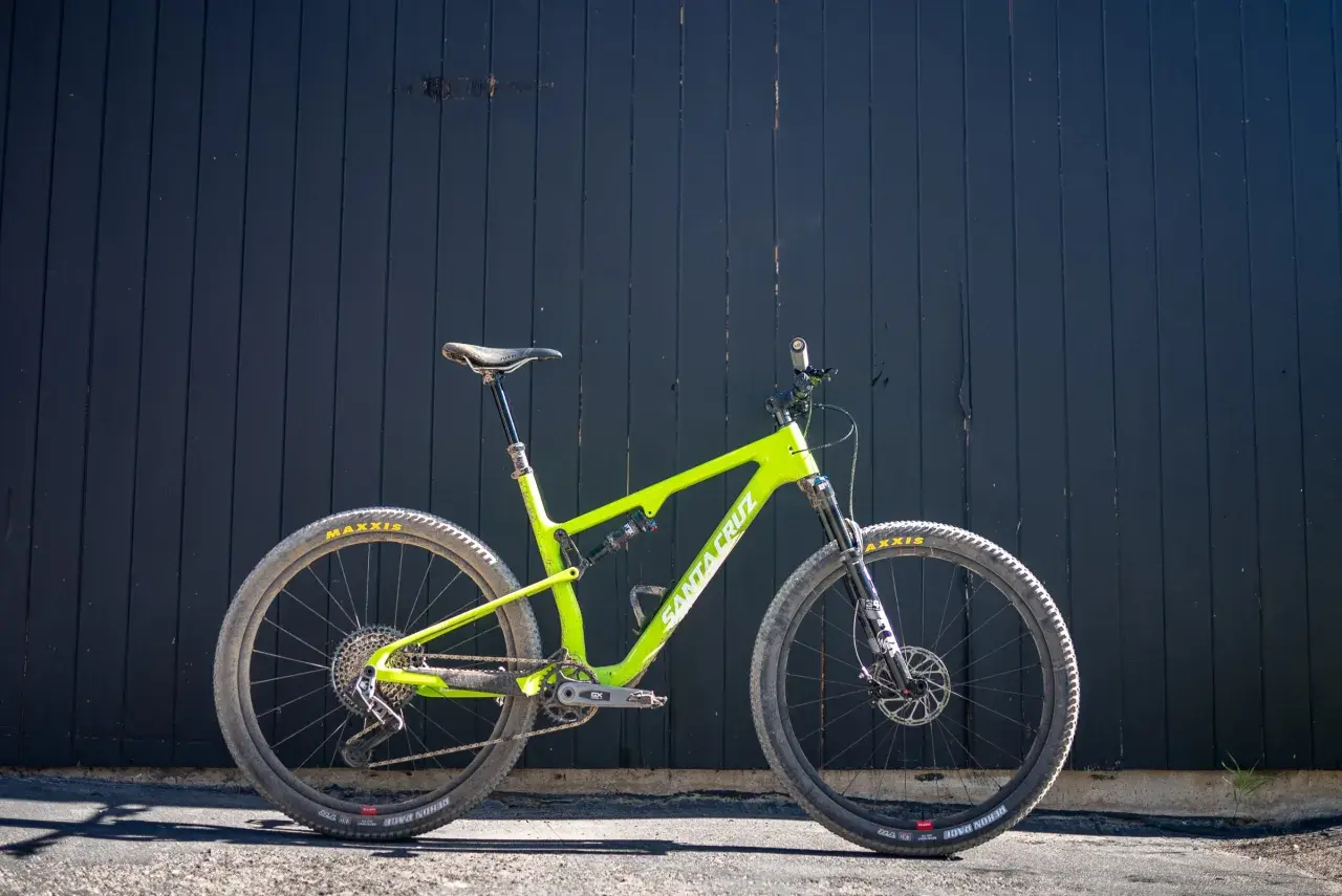 A bright green Santa Cruz Blur mountain bike is ready for a trail review, leaning against a dark wooden wall.