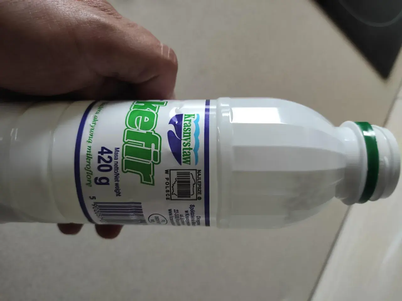Butelka kefiru Krasnystaw 420g, z zieloną zakrętką, trzymana w dłoni.