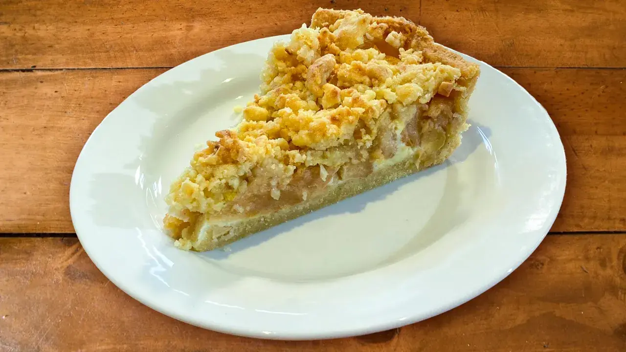 Ein Stück Apfelkuchen mit Streuseln auf einem weißen Teller. Perfekt für ein Apfelkuchen Rezept.