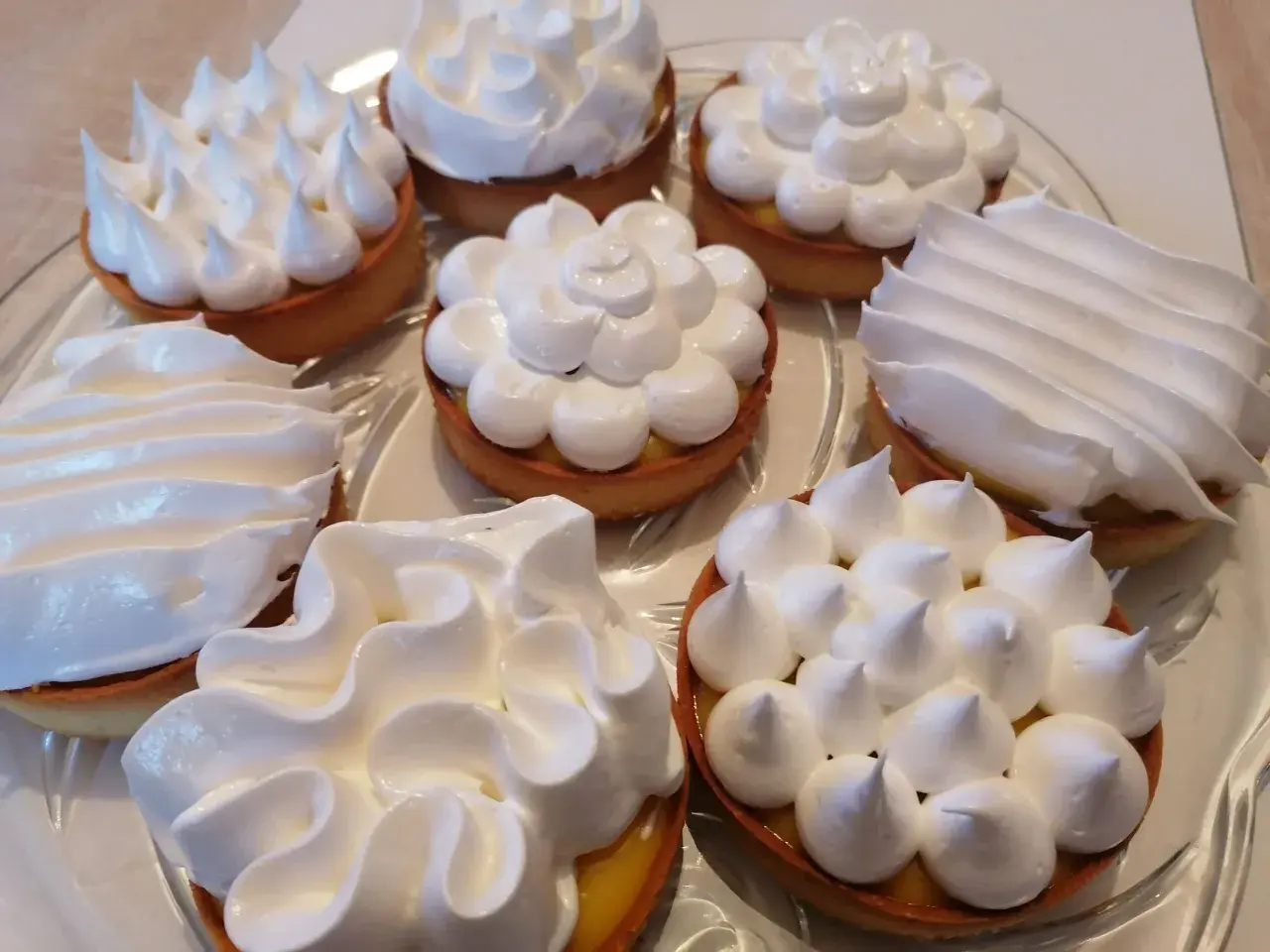 Plusieurs tartelettes garnies d'une crème jaune et surmontées de délicieuse meringue italienne aux formes variées.