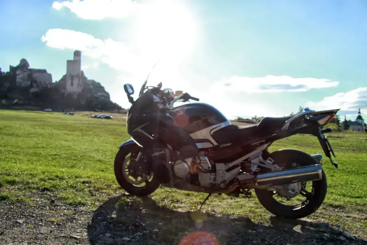 Motocykl na tle zamku i zielonej łąki w słoneczny dzień.