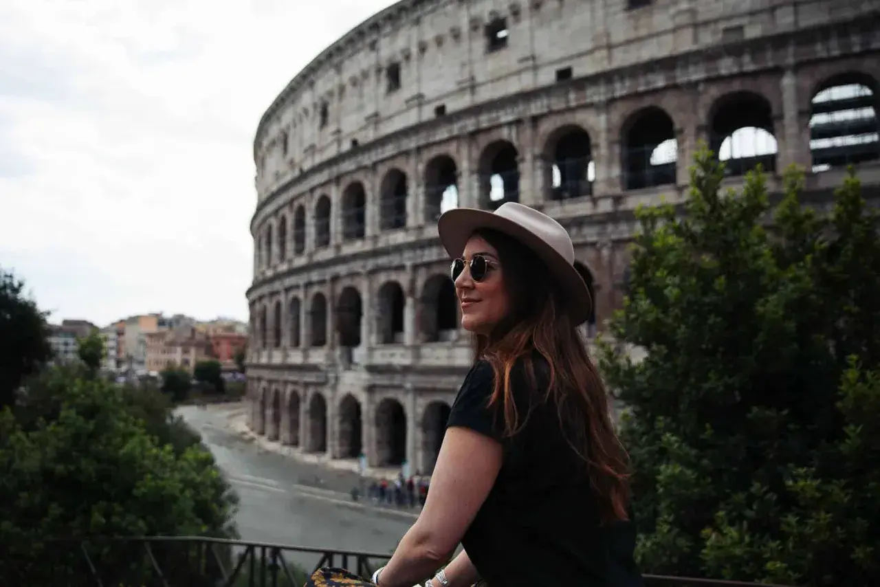 Une femme avec un chapeau et des lunettes de soleil admire le Colisée. Je visite Rome et ce moment est inoubliable.