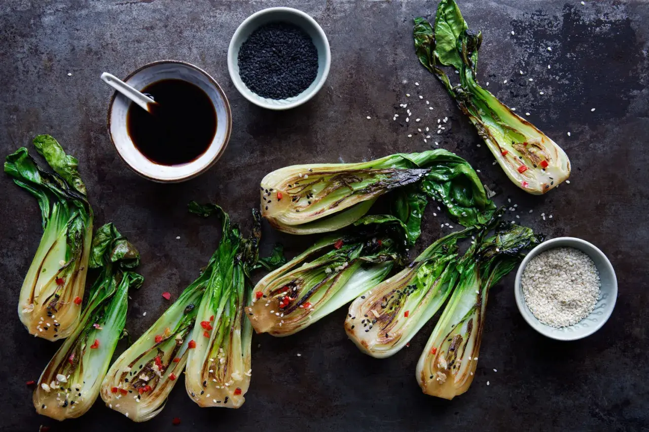 Grillad pak choi med sesamfrön och chili. En skål med sojasås och en skål med svarta sesamfrön syns också.