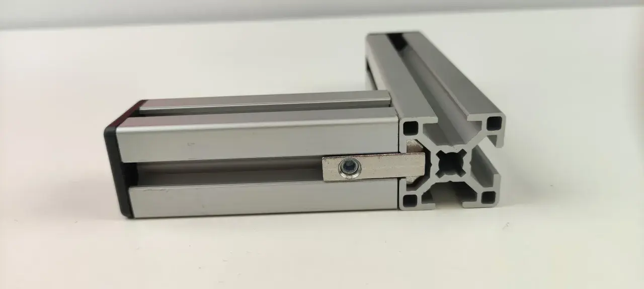 Dwa połączone profile aluminiowe konstrukcyjne tworzą kąt prosty. Widać element łączący z nakrętką.