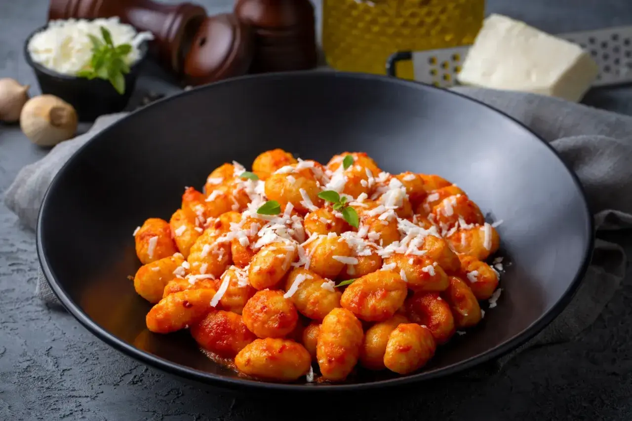 Gnocchi di ceci e patate conditi con sugo rosso e parmigiano grattugiato, guarniti con basilico fresco.
