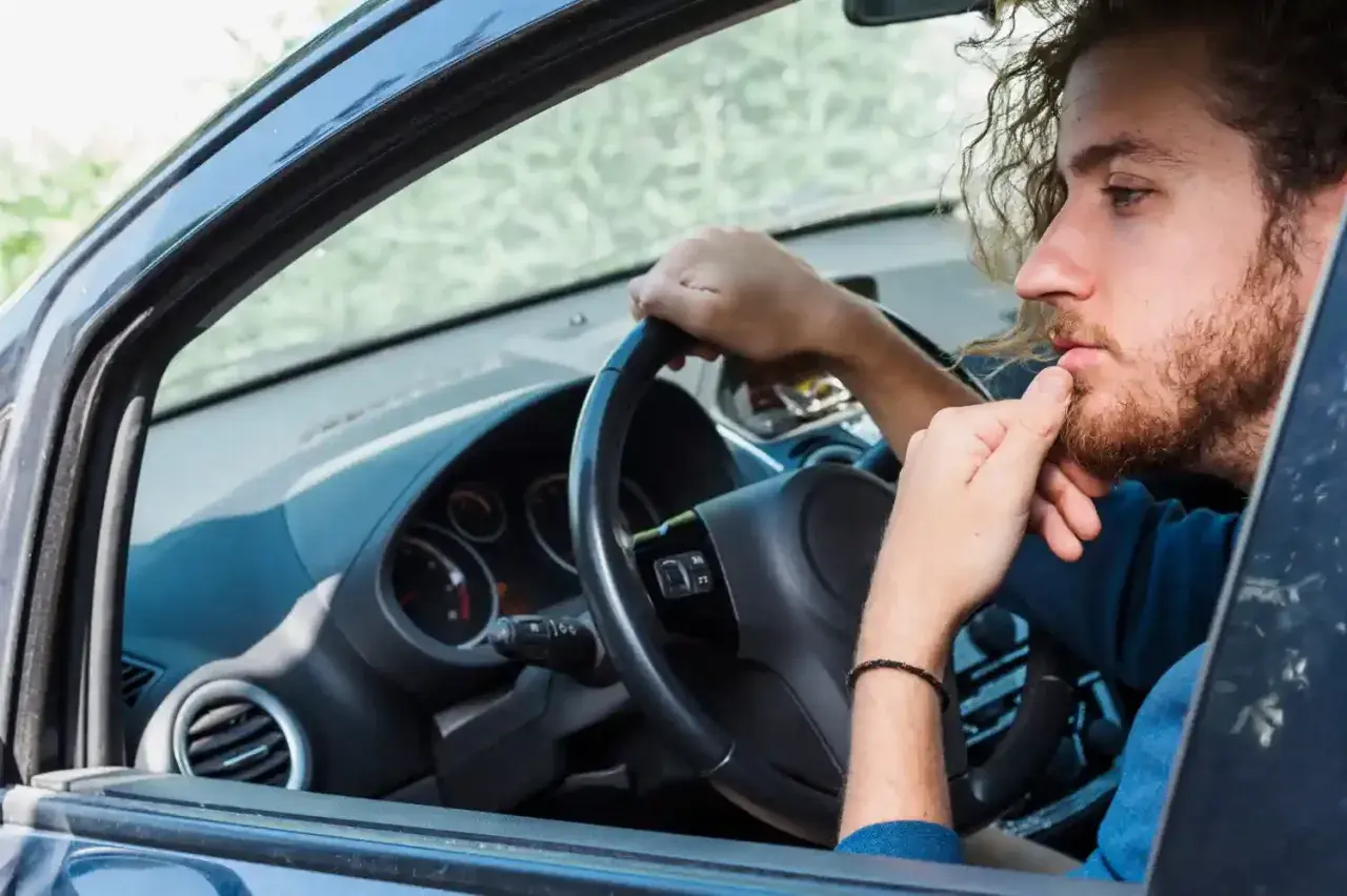 Hombre con barba y pelo rizado, pensativo, con la mano en la barbilla, mientras gira el volante y escucha un **ruido clack clack al girar el volante en parado**.