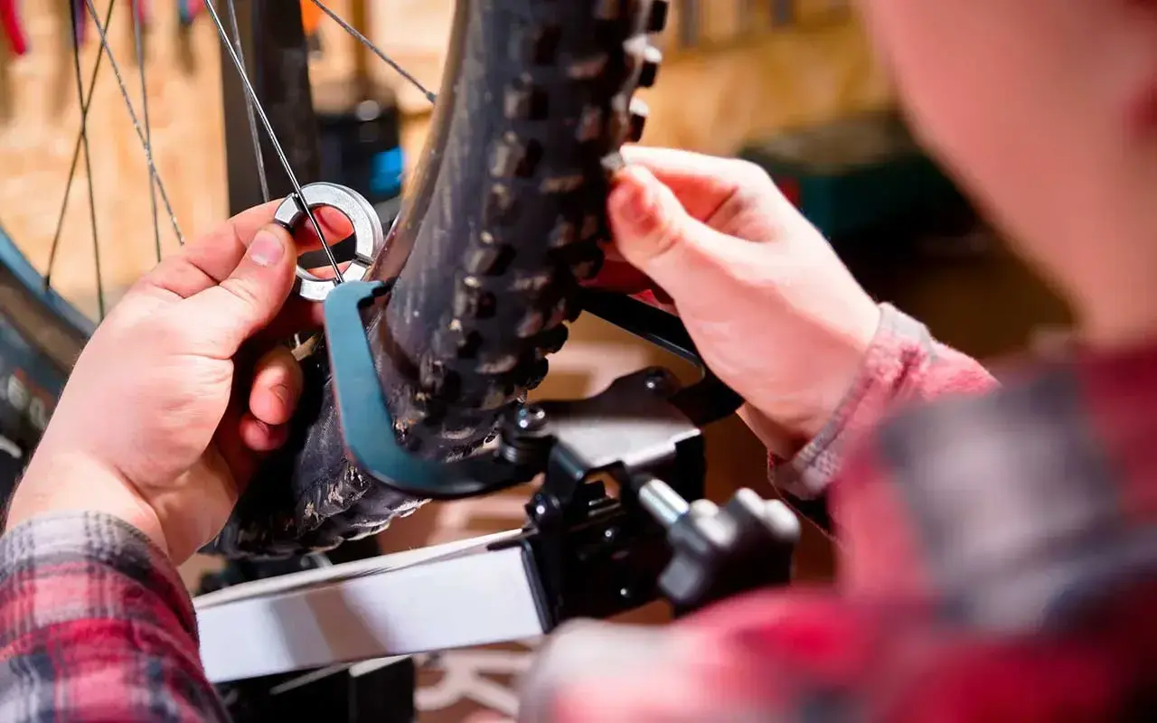 Mains ajustant un outil sur la roue voilée d'un vélo, prêt pour la réparation.