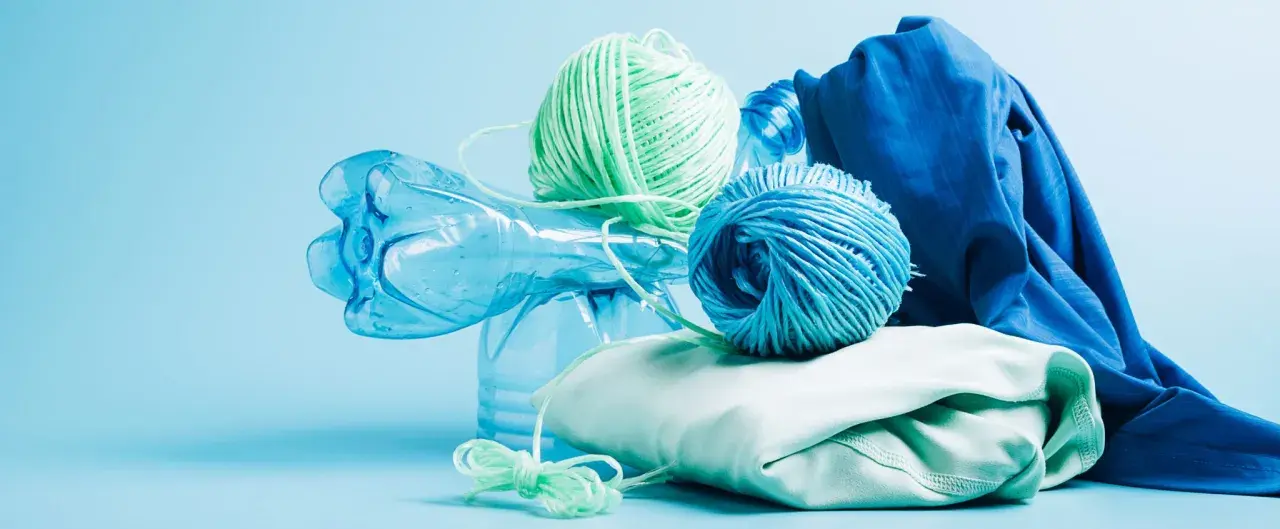 Bouteille en plastique bleue, pelotes de fil vert et bleu, et tissu bleu et vert pâle. Le fil est fait de polyester fiber, prêt à être recyclé.