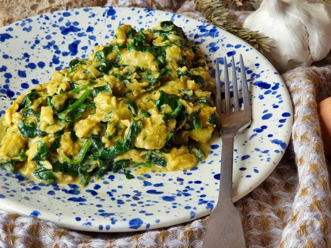 Delicioso revuelto de espinacas cremoso y sabroso, servido en un plato con salpicaduras azules. Un tenedor plateado descansa a su lado.