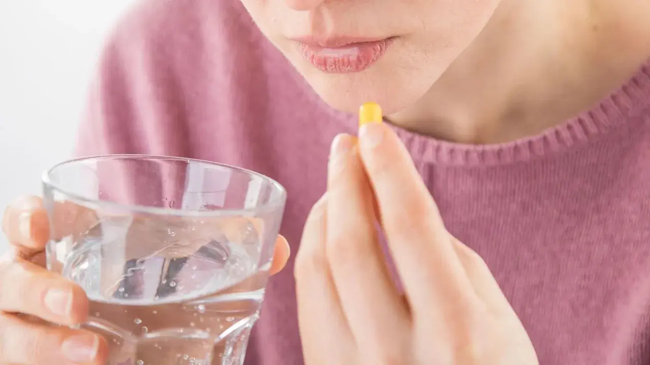 Frau nimmt Kapsel mit Wasser ein, hofft auf Linderung von Tinnitus durch Ashwagandha.