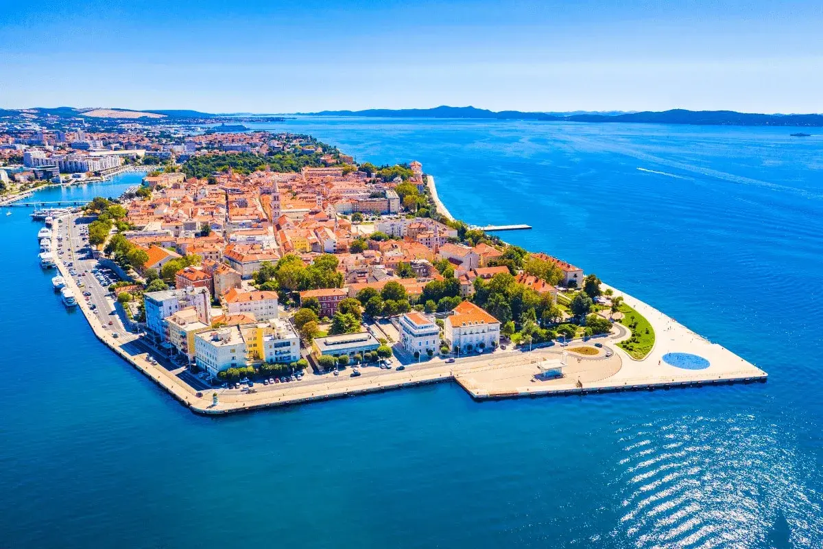 Widok z lotu ptaka na zabytkowe miasto Zadar z czerwonymi dachami, otoczone błękitnym morzem.