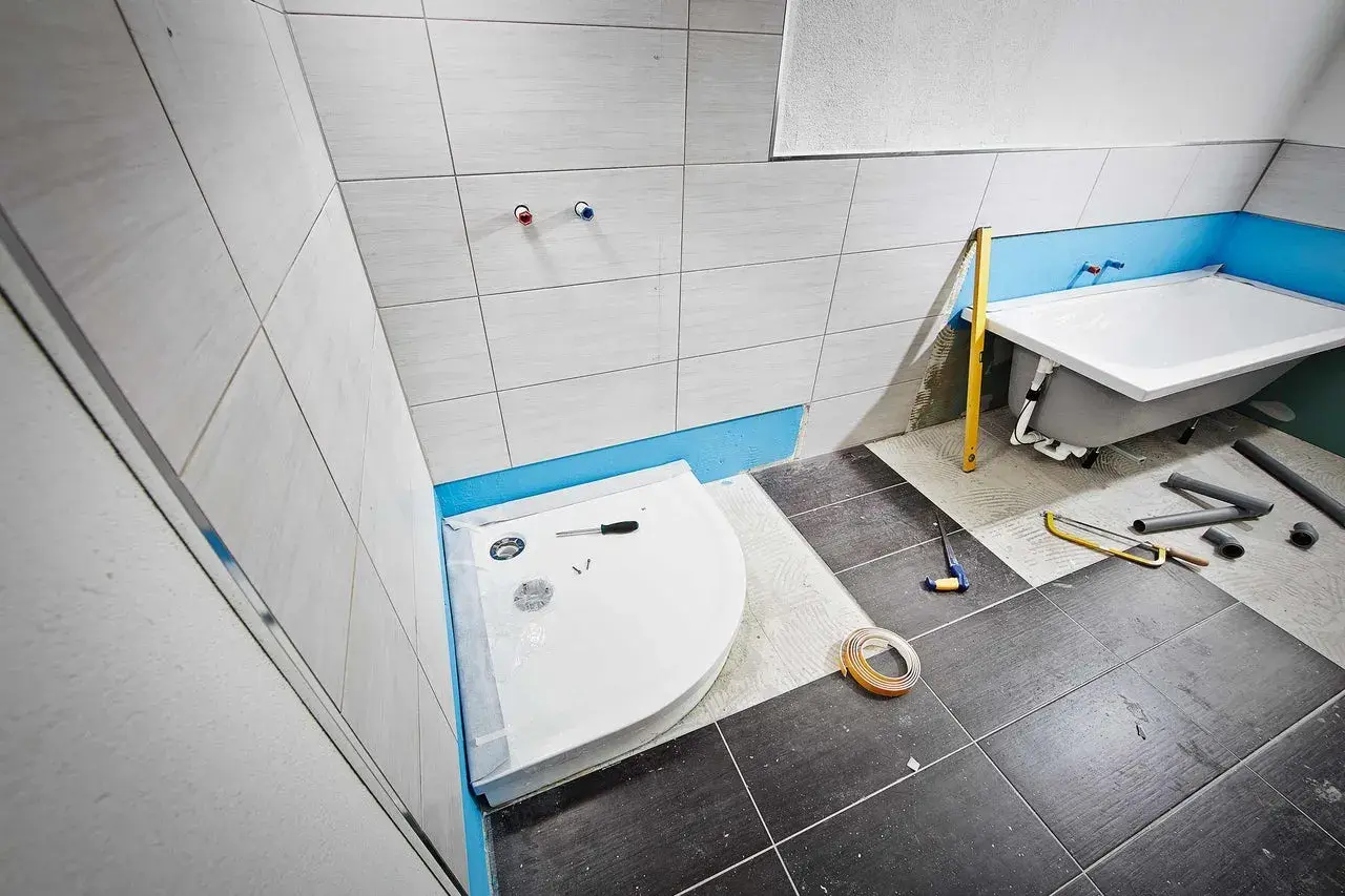 Einbau einer Duschwanne im Badezimmer. Werkzeuge und Rohre liegen bereit.