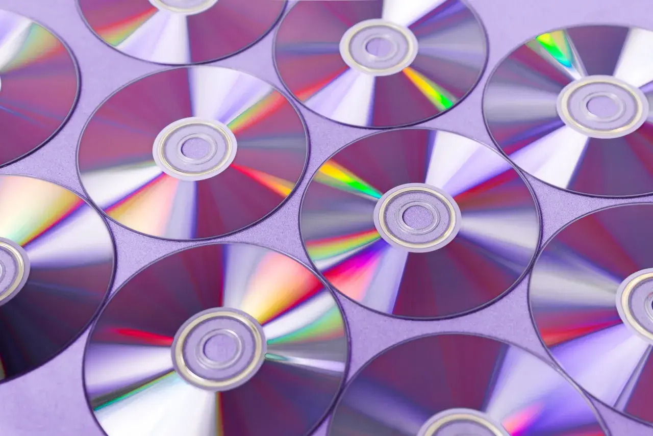 Płyty CD ułożone na fioletowym tle, odbijające światło.