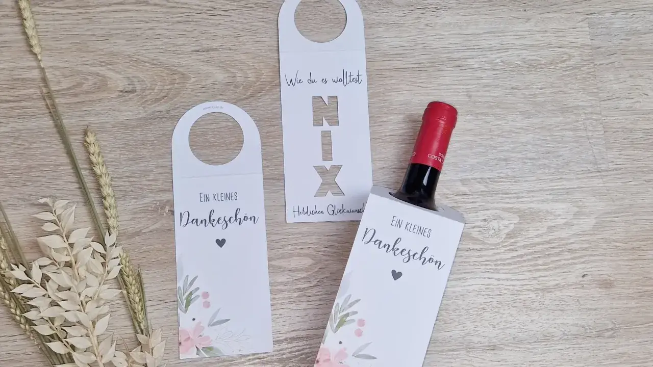 Eine Weinflasche mit Geld verpacken: weiße Hüllen mit floralem Muster und Schriftzug "Ein kleines Dankeschön".