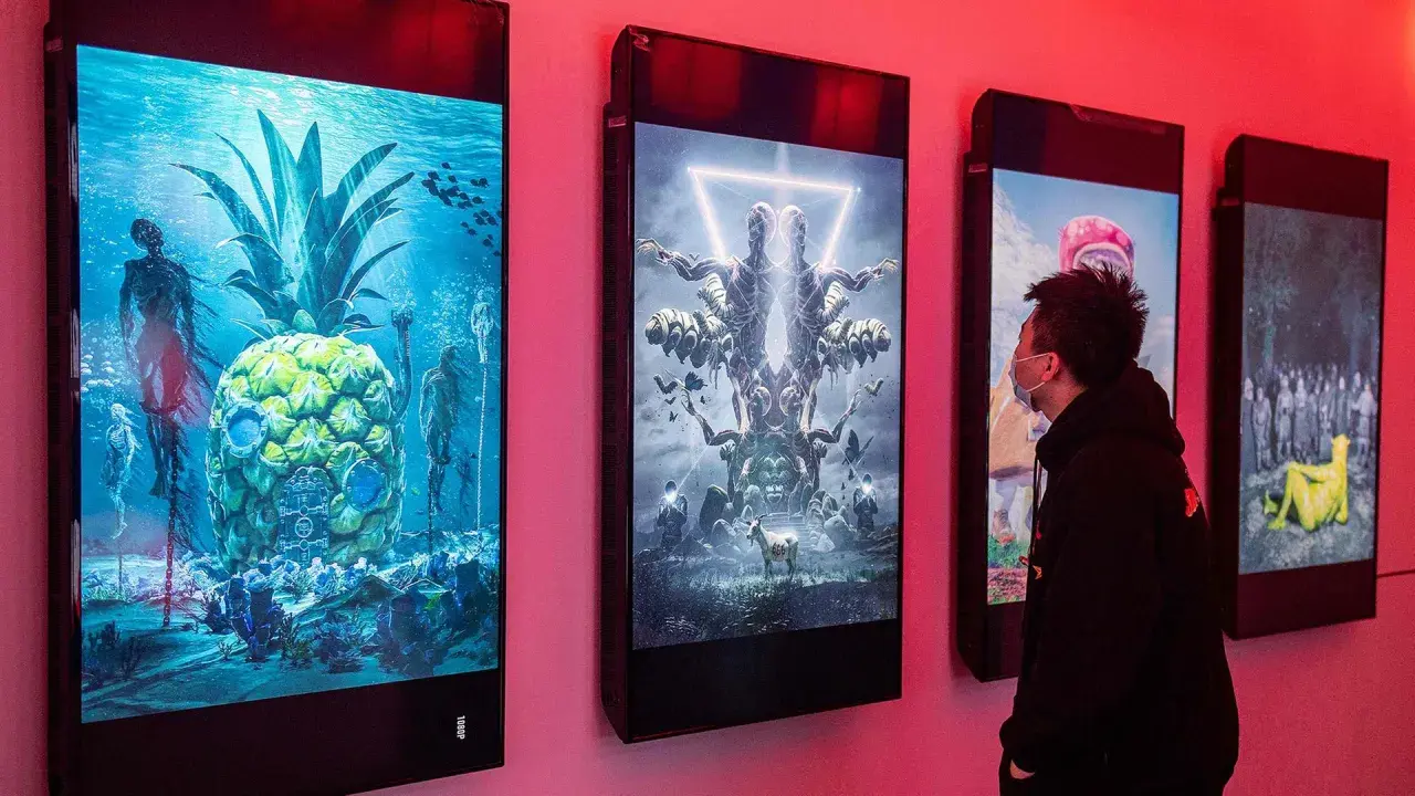 Ein Mann betrachtet digitale Kunstwerke, die an einer Wand hängen. Die Werke zeigen surreale Szenen, wie eine Ananas unter Wasser mit Skeletten und eine symmetrische Figur mit vielen Armen. Diese Werke stammen von einem berühmten Grafik Künstler.