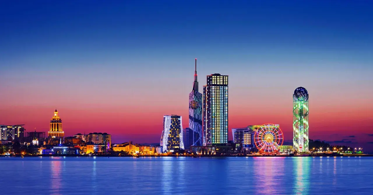 Widok na nowoczesną panoramę Batumi, stolicę Adżarii, o zachodzie słońca. Błyszczące wieżowce i diabelski młyn odbijają się w spokojnej wodzie.