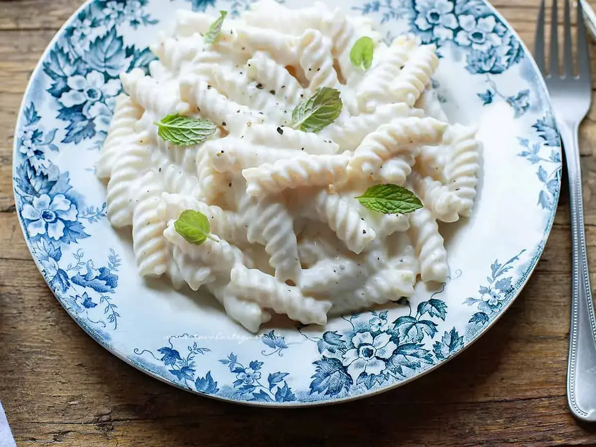 Fusilli cremosi conditi con una salsa vellutata alla ricotta, guarniti con foglie di menta fresca su un piatto decorato.