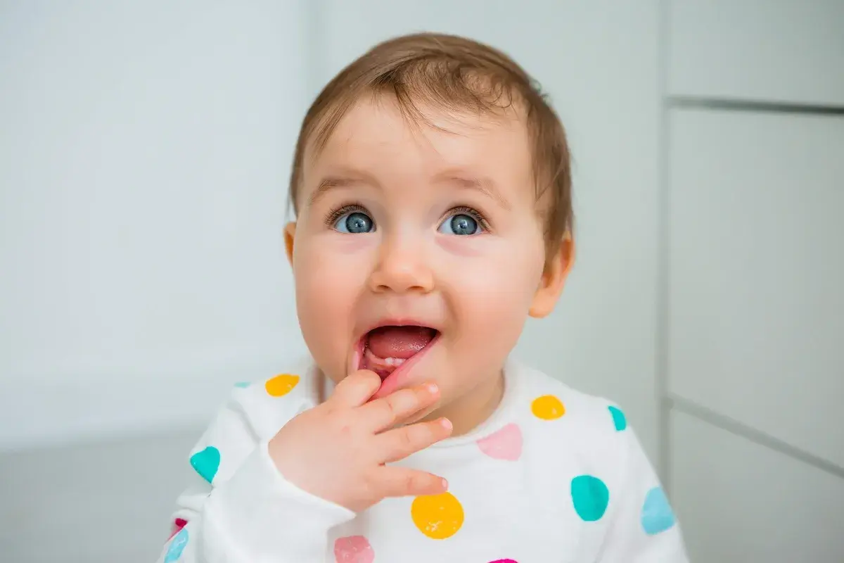 Bambino con dentizione neonato sintomi, che si porta il dito alla bocca con un'espressione curiosa.