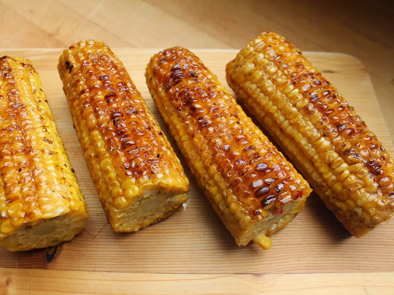 Vier Kolben zuckermais grillen, goldbraun und glänzend, liegen auf einem Holzbrett.