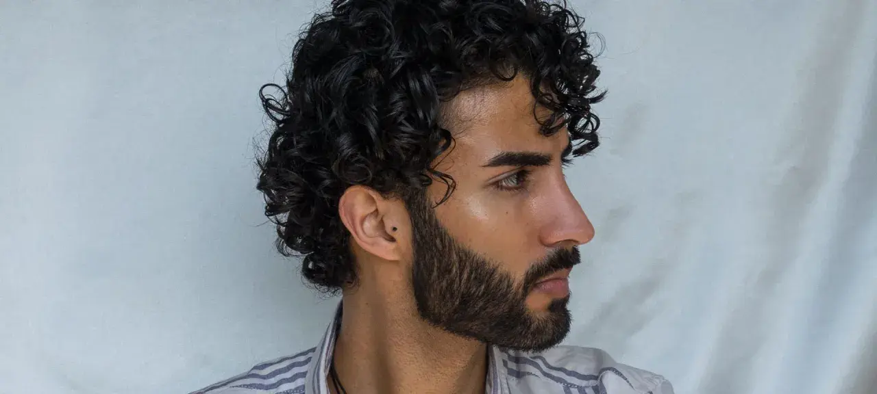 Perfil de hombre con pelo ondulado oscuro y barba cuidada.