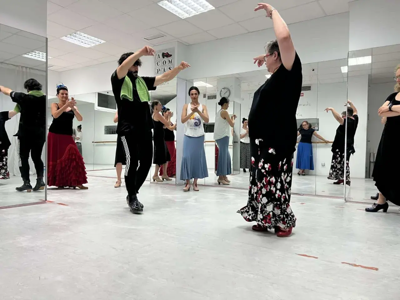 Clase de flamenco facil. Varias personas practican pasos de baile frente a espejos, con movimientos elegantes y faldas amplias.