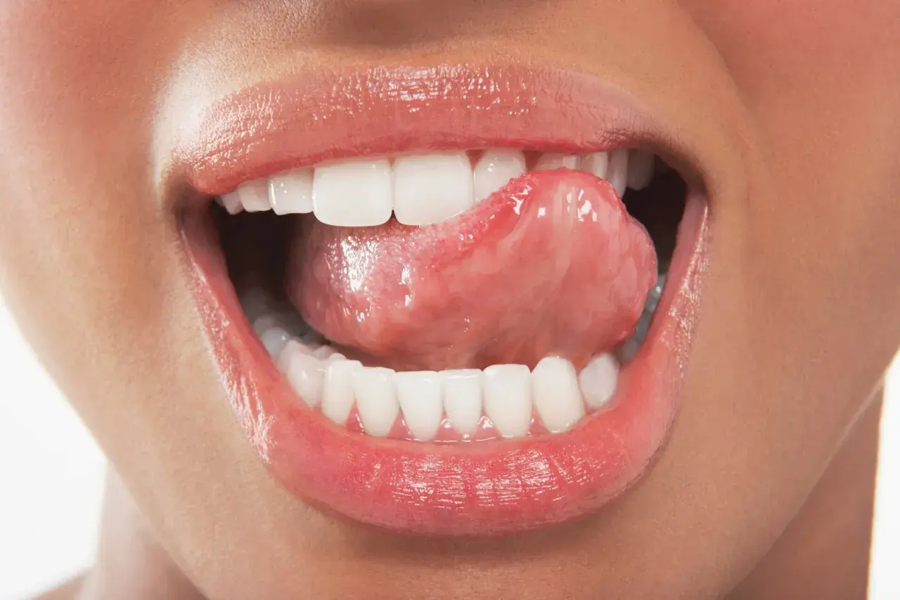 Labbra lucide e lingua che accarezza i denti ruvidi, un gesto sensuale che invita a scoprire.